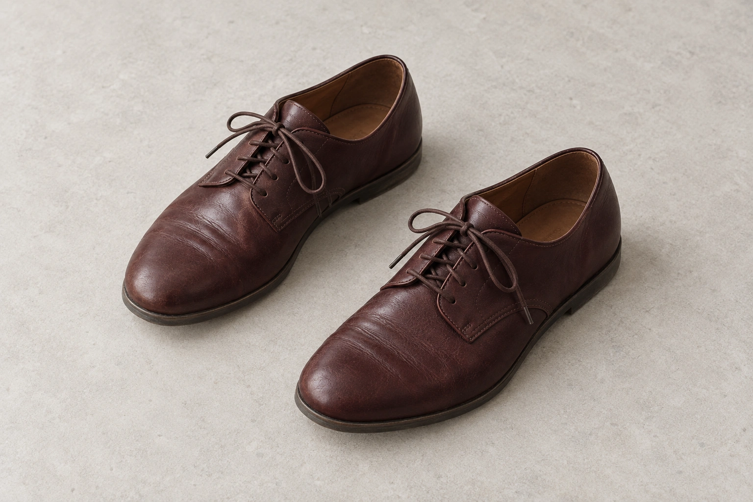 A pair of oxblood-brown leather lace-up shoes on a pale gray stone surface.