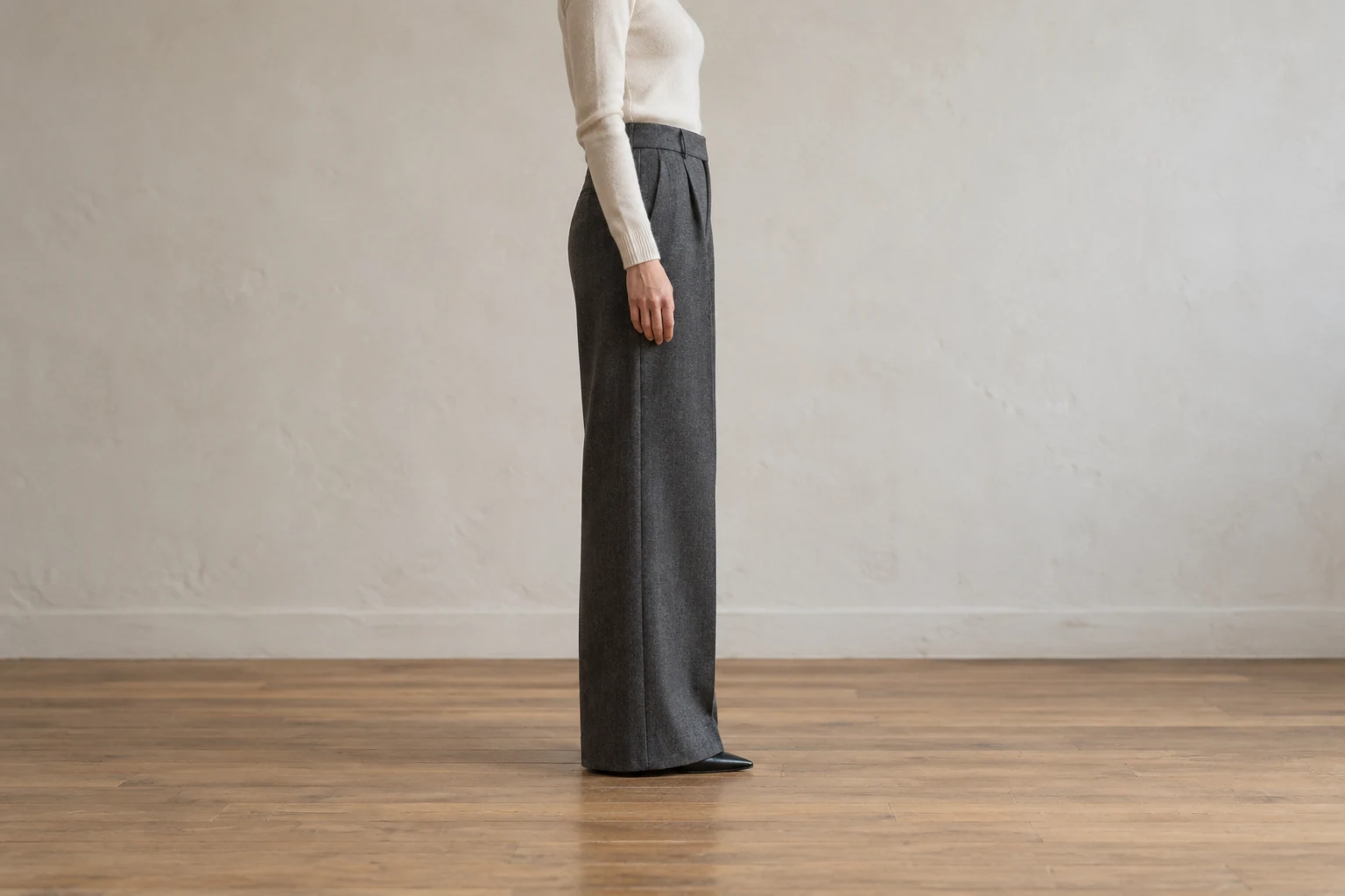 A side view shows charcoal wide leg trousers ending just above the floor with one pointed pump toe visible.