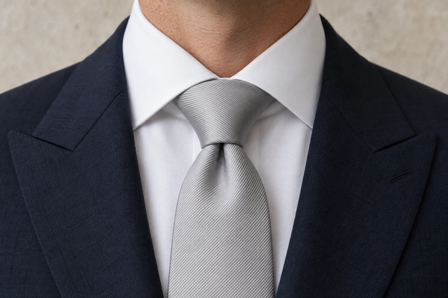 A broad silver silk full Windsor knot fills a white cutaway collar between navy peak lapels