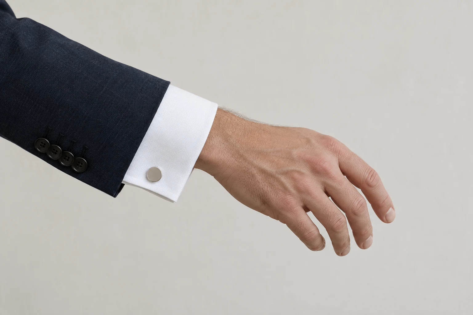 A relaxed hand extends from a navy jacket with a white French cuff secured by a round silver cufflink.